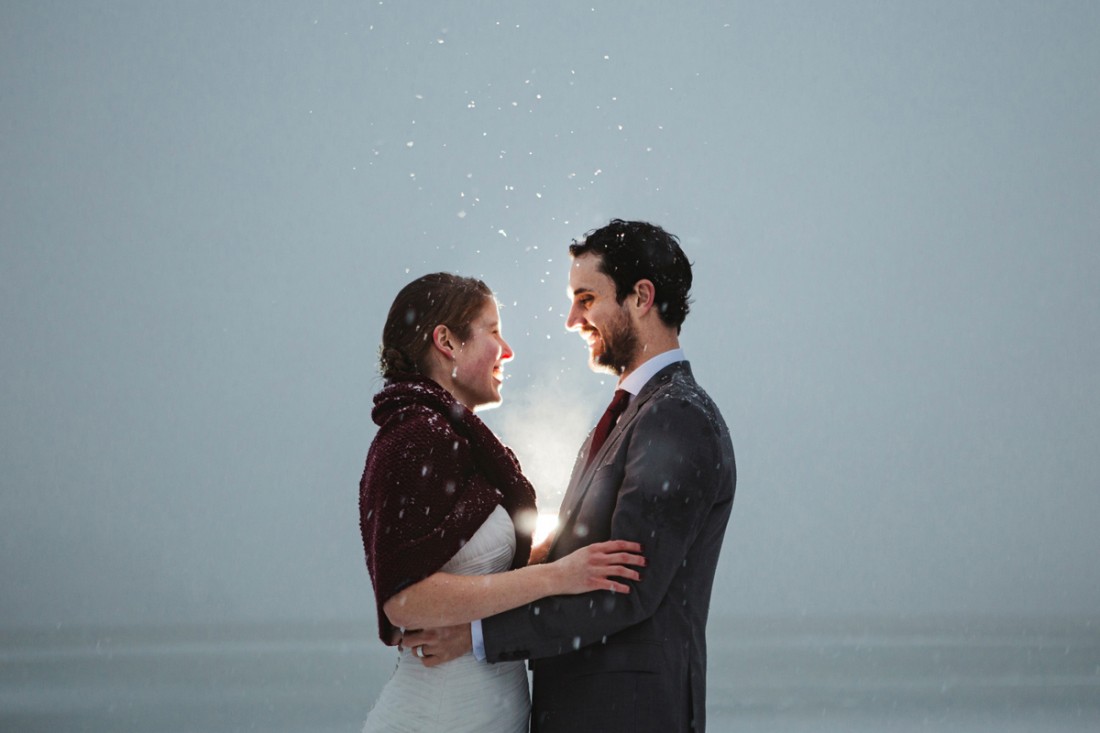Couple in front of an icy lake under sunset light with flying shinning snow flake after their wedding ceremony in edgewater lodge, Whistler
