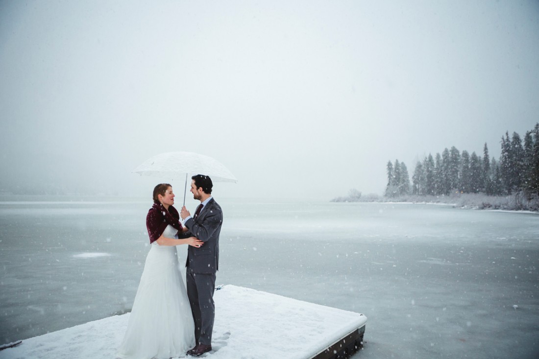 Couple in front of an icy lake under sunset light with flying shinning snow flake after their wedding ceremony in edgewater lodge, Whistler