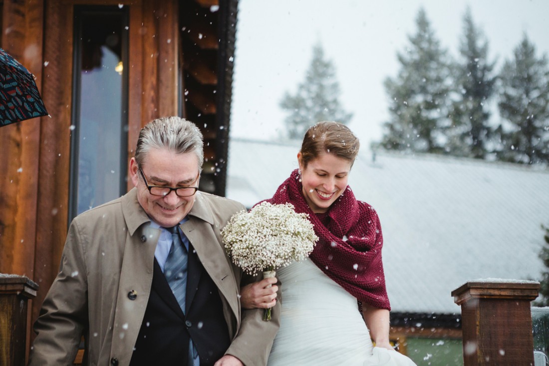 bride walking down stairs towards the backyard of edgewater lodge whistler under the snow holding by her father