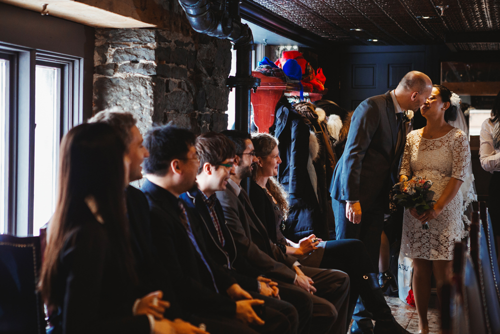 bride and groom kissing while guests sitting in a row looking at them in their ceremony and reception hall in vieux port steakhouse, Montreal