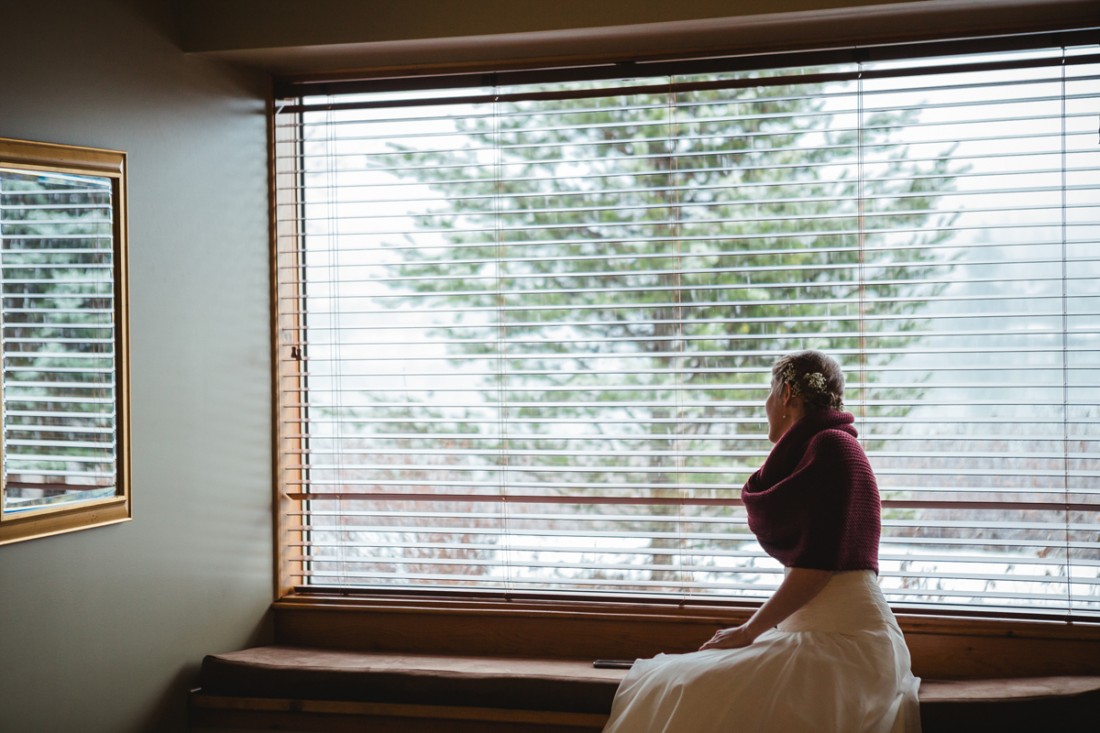 bride looking through the window and waiting for her father to pick her up for the outdoor ceremony in edgewater lodge, whistler